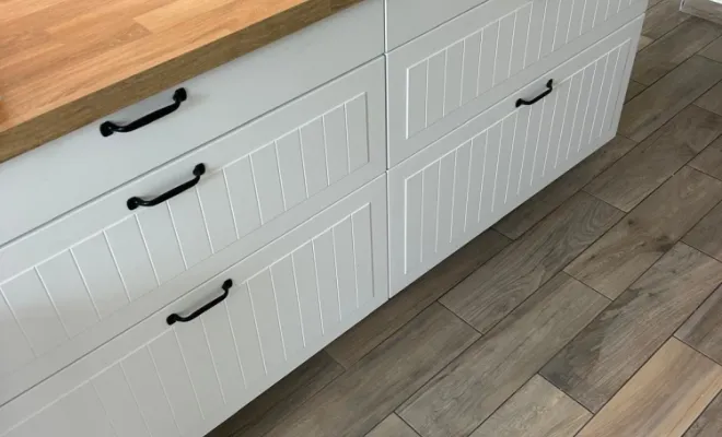 Menuiserie : Montage et pose de caissons de cuisine avec ajustement de précision des façades travaillées pour un alignement horizontal parfait. Installation de poignées noires sur mesure.  Plan de Travail : Pose d'un grand plan de travail en chêne, ajusté avec des coupes nettes pour les contours de la pièce.  Sols : Pose d'un carrelage imitation bois avec joints assortis, nécessitant une préparation de sol (ragréage éventuel) pour une planéité parfaite, assurant durabilité et facilité d'entretien.